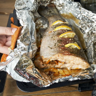 Trout fish freshly baked in a foil with lemon slices and vegetables in an electric oven